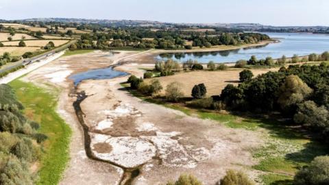 An aerial image of Chew Valley Lake shows the water level exceptionally low, with much of the dry lake bed exposed. The lake is surrounded by brown fields.
