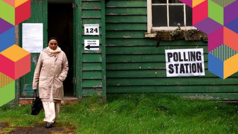 A woman outside a polling station in a green wooden hut
