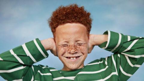 A smiling boy covering his ears with his hands.