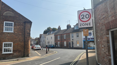 A 20mph zone sign on a post in Fordington. The narrow streets are lined with old terraced houses.