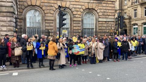 A line of people holding banners and posters of family members stood in a line on the pavement outside Liverpool Town Hall