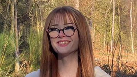 Brianna Ghey wearing large spectacles and smiling while surrounded by trees