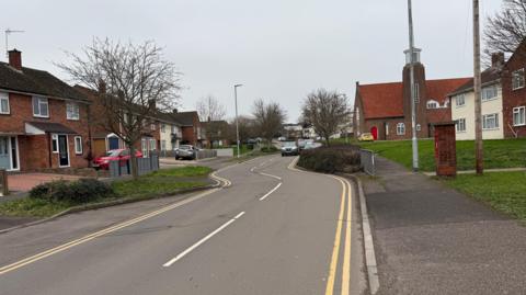 Two cars drive down the chicanes on Eastwick Road in Taunton with houses either side. It is a two-lane road with double yellow lines each side