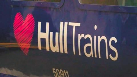 A close-up of the side of a dark blue train carriage with a large logo reading "Hull Trains" in white text, next to a pink heart. A train serial number reads "50911".