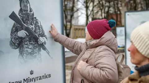 A woman touches a memorial photo of a soldier as she attends a gathering to observe a moment of silence to pay tribute to victims of the Russia war