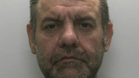 A close-up of Lee Blatchford who has a brown and grey short beard and brown and grey hair. He is directly into the camera and is not smiling.