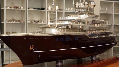 Elaborate model of a boat on a wooden stand. The bottom of the boat is carved from wood and the top, including the deck, radar and cabins are silver-coloured. 
