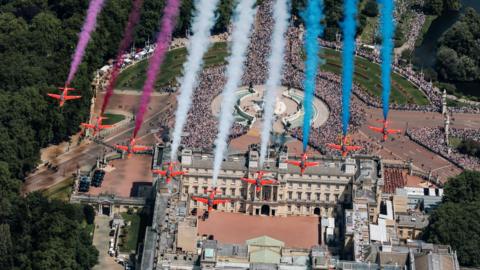 View from above as nine Red Arrows jets fly over Buckingham Palace trailing red, white and blue smoke behind them