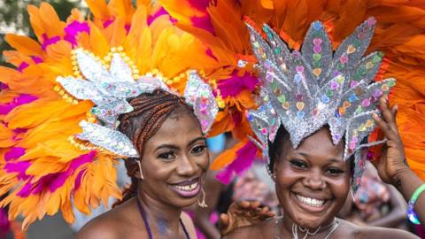 Two women in headdresses made of silver material and orange and pink feathers smile at the camera at the carnival in Calabar, Nigeria