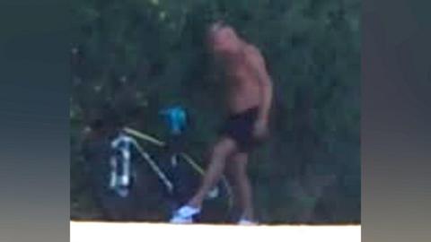 A blurry CCTV image showing a topless man in black shorts standing next to a lime green coloured bike.