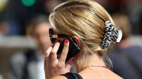 A woman with blonde hair and sunglasses can be seen holding a mobile phone to her ear.