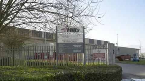 The exterior of the Northacre Mechanical Biological Treatment plant. It is a large grey building with a grey metal fence around the exterior