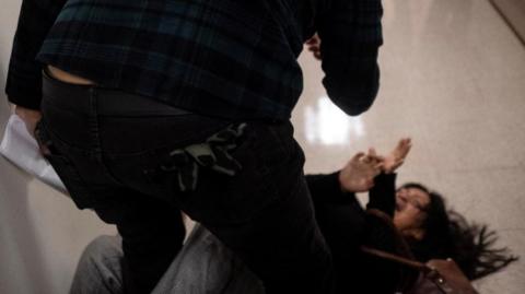 A man hunches over woman a woman lying on the floor. 