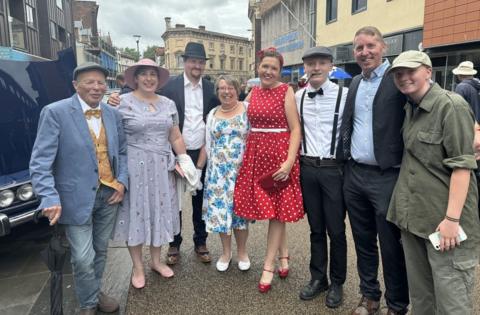 A group of people in vintage outfits line up alongside buildings in Gloucester city centre