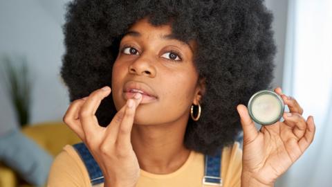 A woman applying lip balm with her finger.