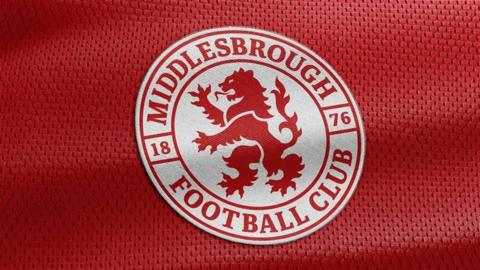 The new badge which is a white circle with a red lion in the centre of it. 'Middlesbrough Football Club' is written in red letters around the circle, with the year 1876. The badge is sitting on what looks like a red sports shirt.