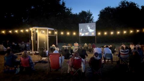 An audience watches a movie in a field