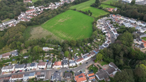 Aerial shot of properties in Jersey. A road runs through a row of houses. A large green field is behind the properties.