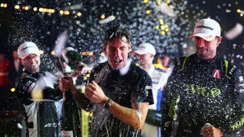 Ian James, Team Principal of Jaguar TCS Racing celebrates winning the team championship on the podium during the London E-Prix, Round 17 of the 2026 FIA Formula E World Championship at ExCel London on 16 August 2026. He has popped a bottle of champagne which is spilling around.