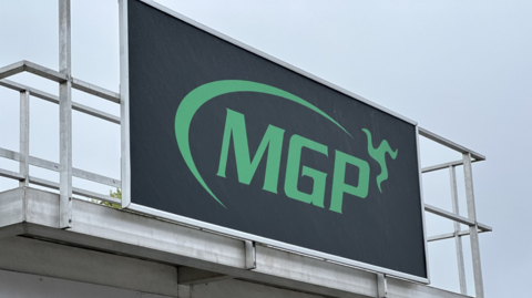 The podium at the grandstand fronted with a large signage board that has the MGP logo in green on a black background.