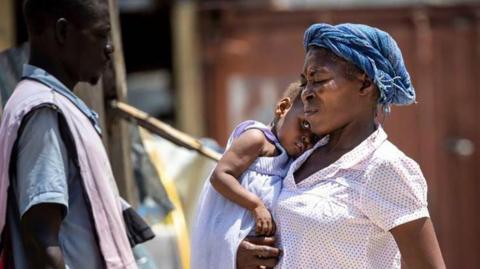 A woman carries a child across the school yard at Ecole National Joseph C. Bernard DeFreres displacement camp on Aug. 27, 2024, in Port-au-Prince, Haiti. 