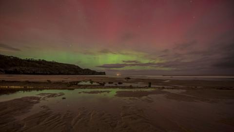 Red and green Northern Lights display above a dark beach