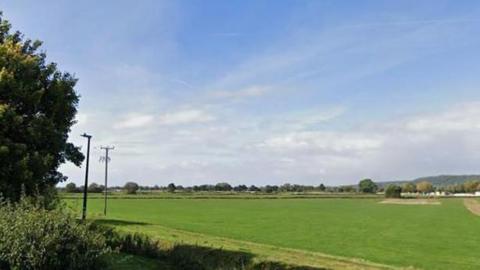 A green field with telephone pylons underneath a clouded sky