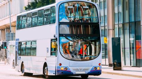 A double decker grey and purple bus in a city centre