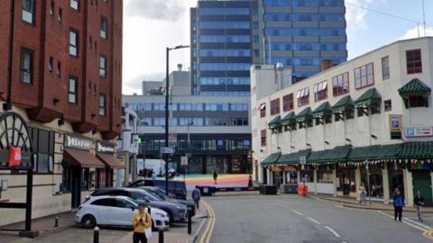 A street view of Ladywell Walk with buildings on either side of the road and high-rise flats in the background.