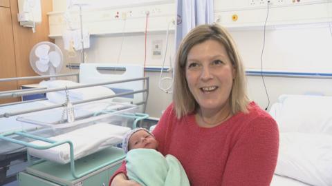 a baby in a green blanket held by a woman in a red pullover