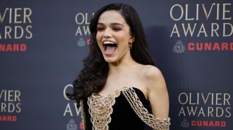 Rachel Zegler in black dress adorned with gold chains