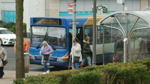 Bus at a stop in Corby Town centre with people walking past.