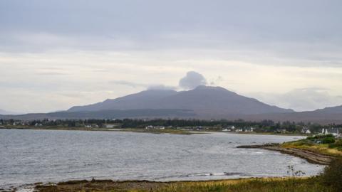 An island bay pictured on a slightly cloudy afternoon with a mountain in the background.