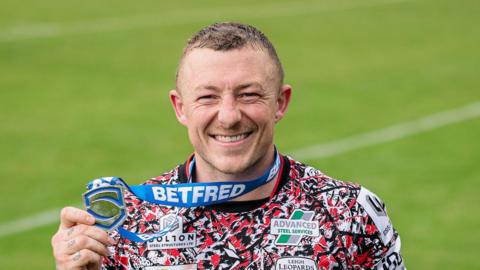 Josh Charnley holding up a silver Player of the Match award in his right hand while it's hanging around his neck following Leigh's win at Bradford