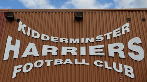 A sign on the exterior of Aggborough Stadium reads 'Kidderminster Harriers Football Club' in white font
