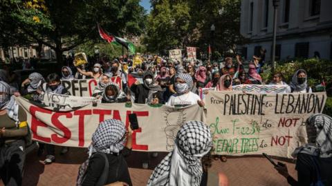 A group of students wearing keffiyehs and holding Palestinians flags at a protest at Columbia University in New York