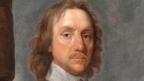 A 17th Century portrait of Oliver Cromwell, with shoulder-length curling mid-brown hair and moustache, wearing a white lace collar done up at the neck over a yellow under-jacket, above which is grey armour. He looks at the viewer with dark eyes.