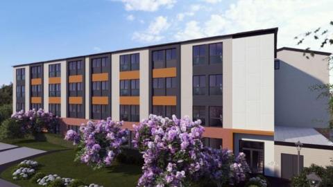 An artist's impression of the new accommodation block at Hinchingbrooke Hospital. It is a flat-roofed four-storey building with large black windows against white and orange walls. In front of it are shrubs with pink flowers. 