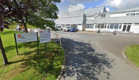 The image shows an orange and white sign which says DS Smith, behind which can be seen a white and grey industrial building with a tree and grass to the left.
