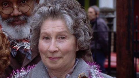 A woman with curly grey hair looks at the camera
