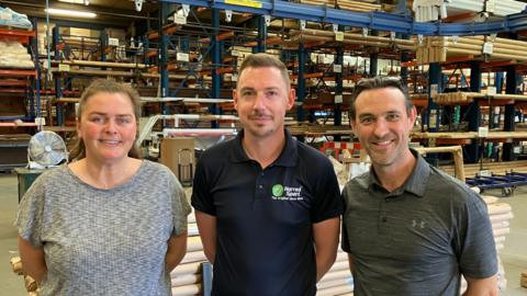 Three people smiling and standind beside each other in a factory setting