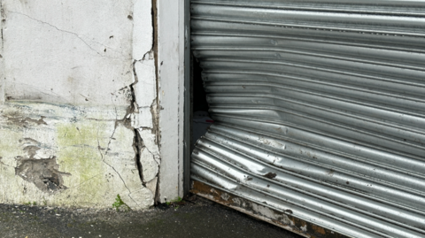 A close-up of a large dent in a metal garage barrier. There is also damage to the wall located on the left.