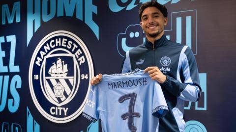 Omar Marmoush holding a Manchester City shirt with the number seven on the back 