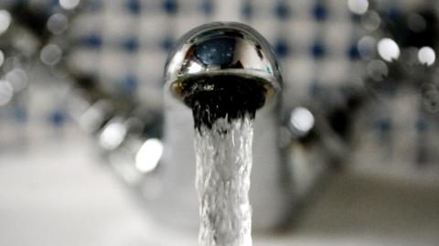 A close up of a silver tap with running water coming out of it.