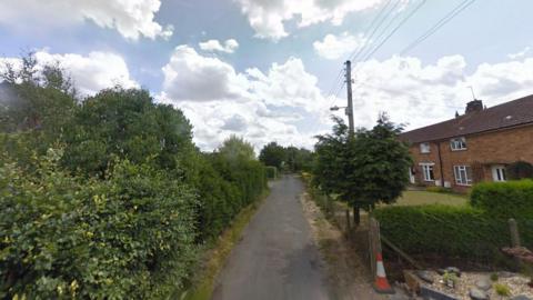 Church Lane in Snitterby. A narrow lane with bushes either side and some terraced house can be seen on the right.