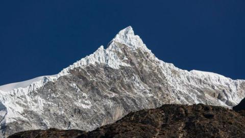 A panomanic view of the Langtang Lirung peak. The snowy summit is seen against a clear blue sky.