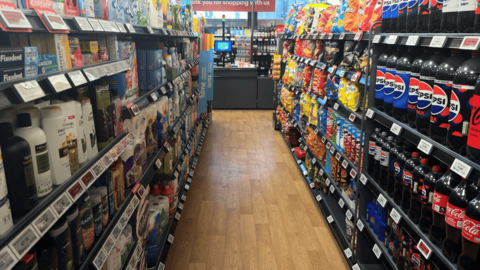 Shop isle with Shampoo, toothpaste on one site and food and drink on the other 
