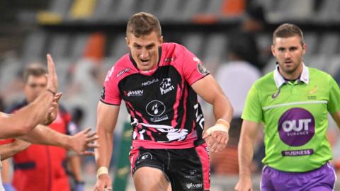 Stefan Coetzee kicks a ball forward and chases after it as a touch judge watches on behind him