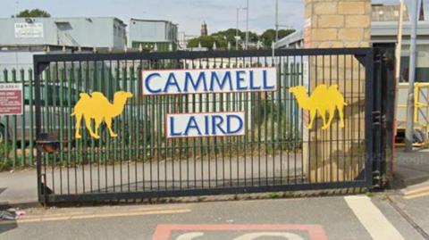 Cammell Laird gates, painted black with two yellow silhouettes of camels and the company's name in blue writing on a white background