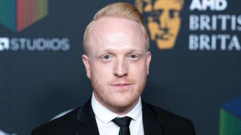  Owain Rhys Davies wearing a black blazer, black tie and white shirt.